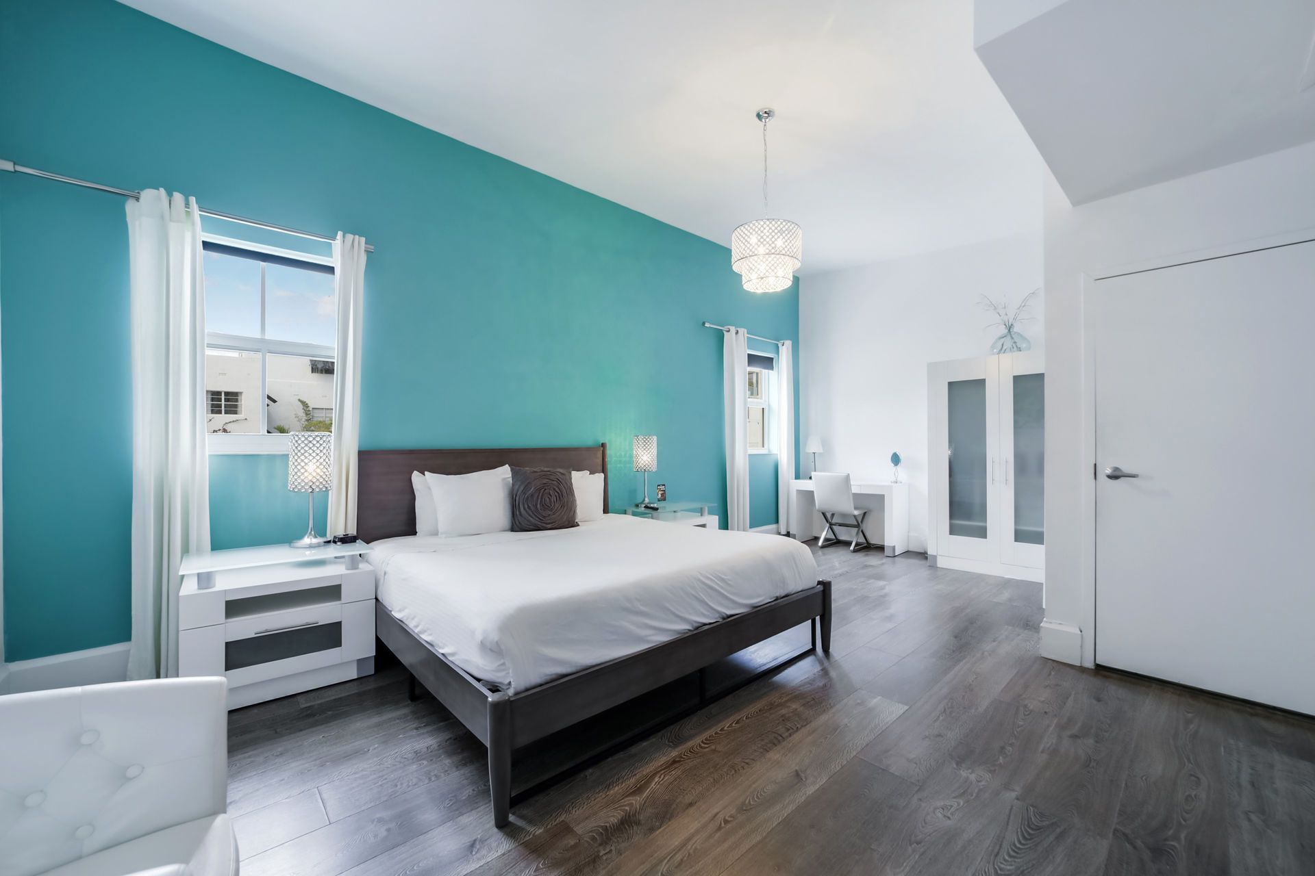 Bedroom with a turquoise accent wall, gray bed frame, and wooden floors.