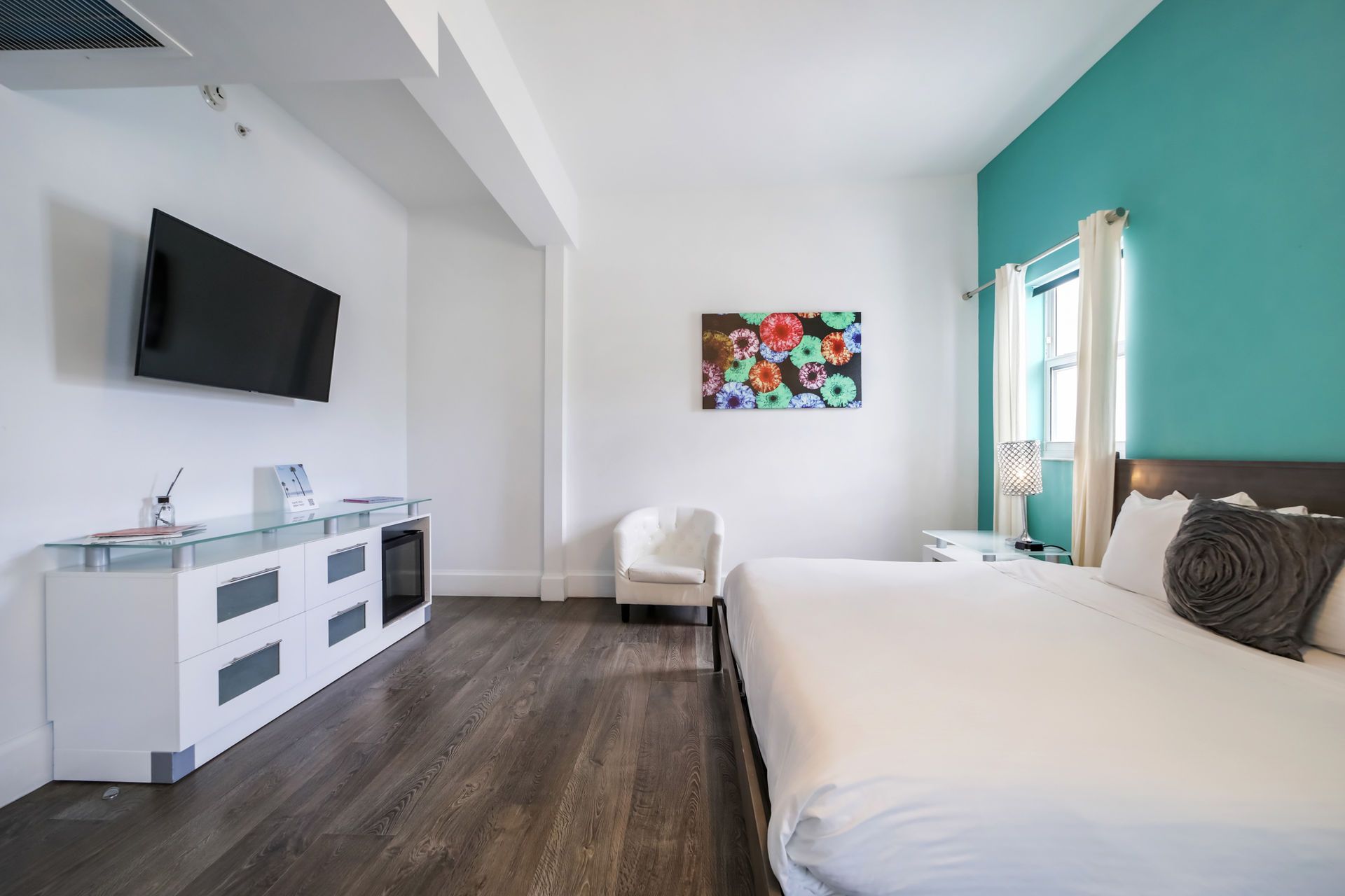 Bedroom with a bed, TV, white cabinets, artwork, and turquoise wall.