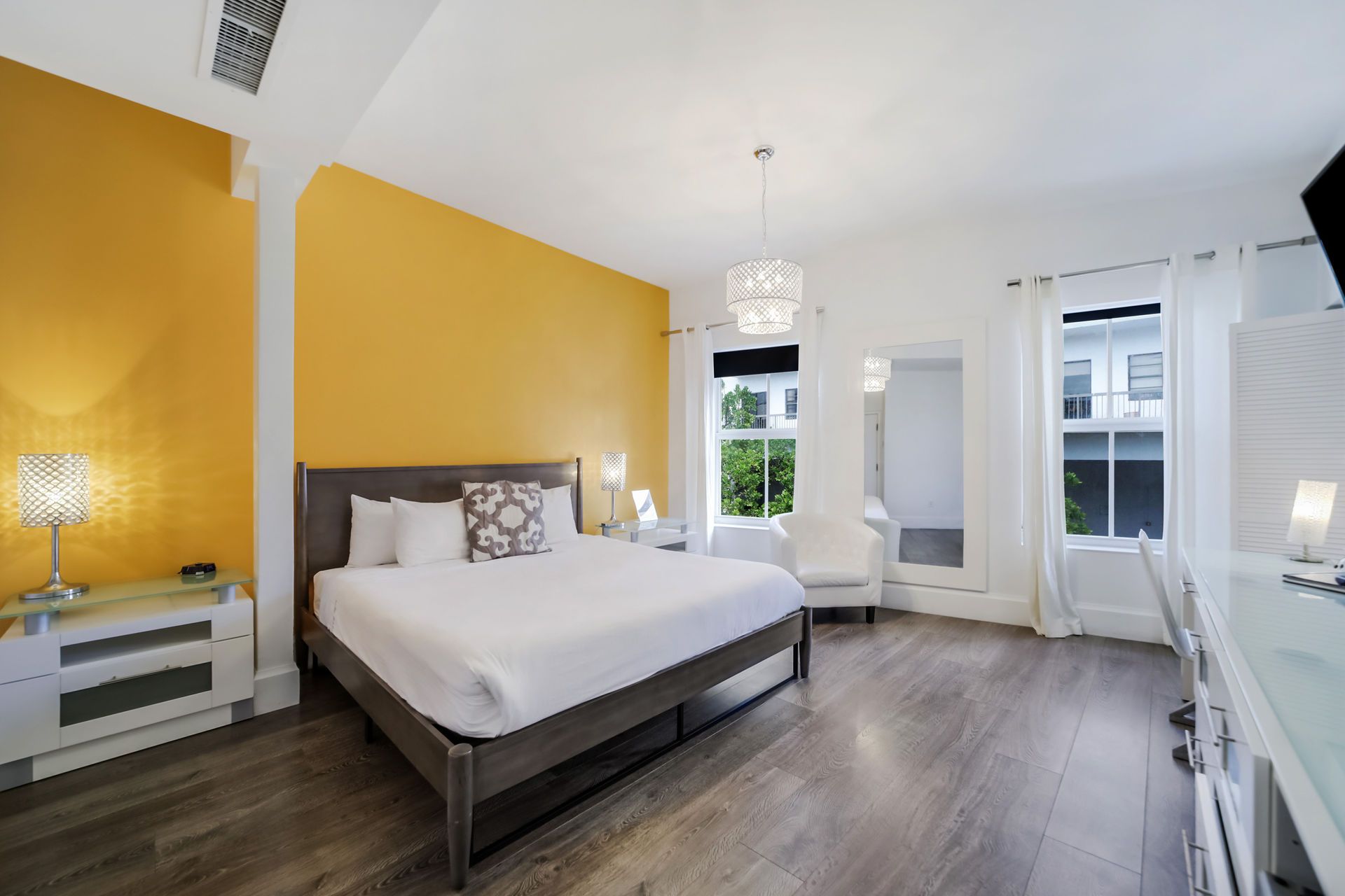 Bedroom with a king bed, yellow accent wall, and white trim; bright and airy.
