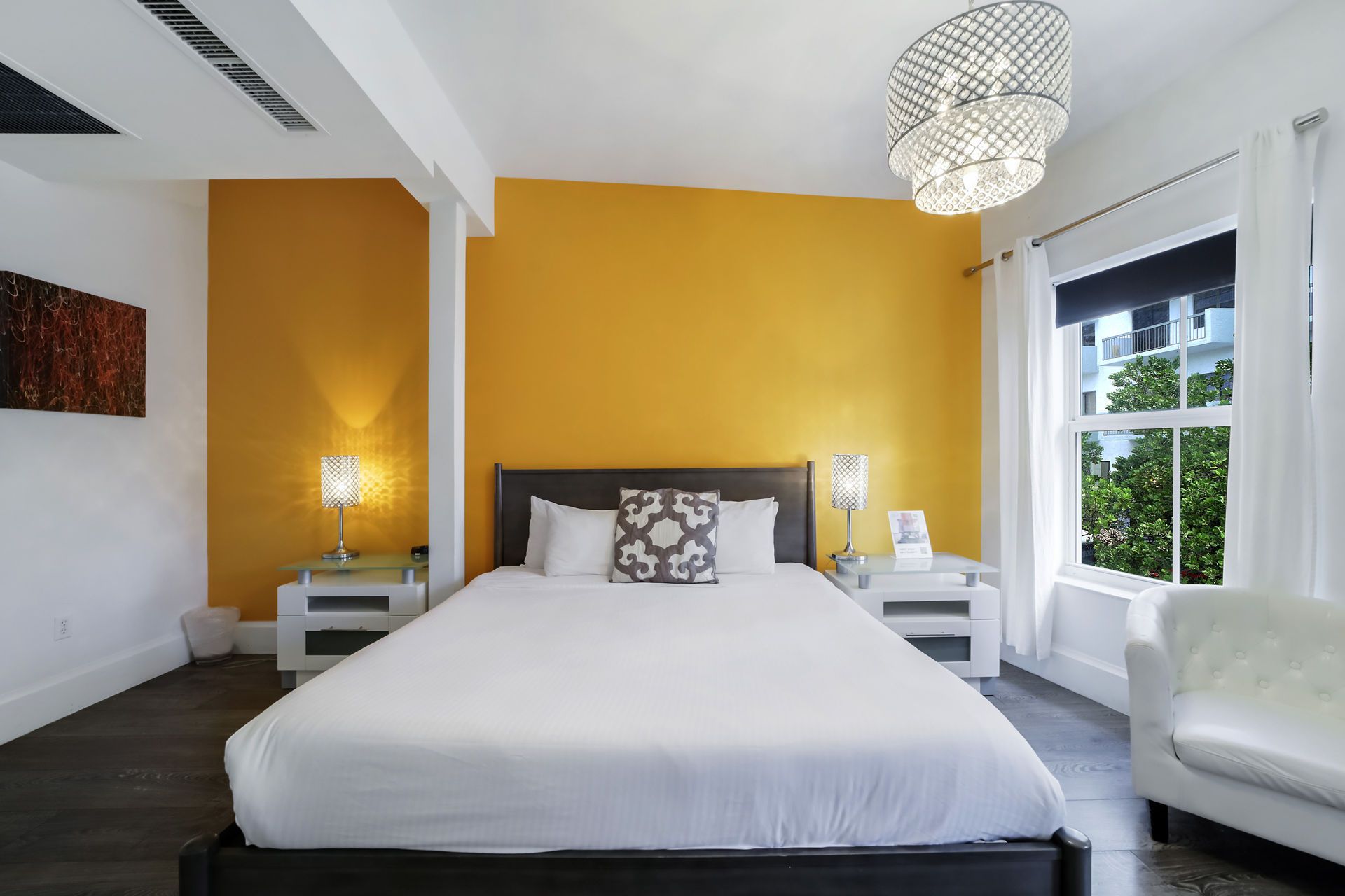 Bedroom with yellow accent wall, white bedding, nightstands, and chandelier.