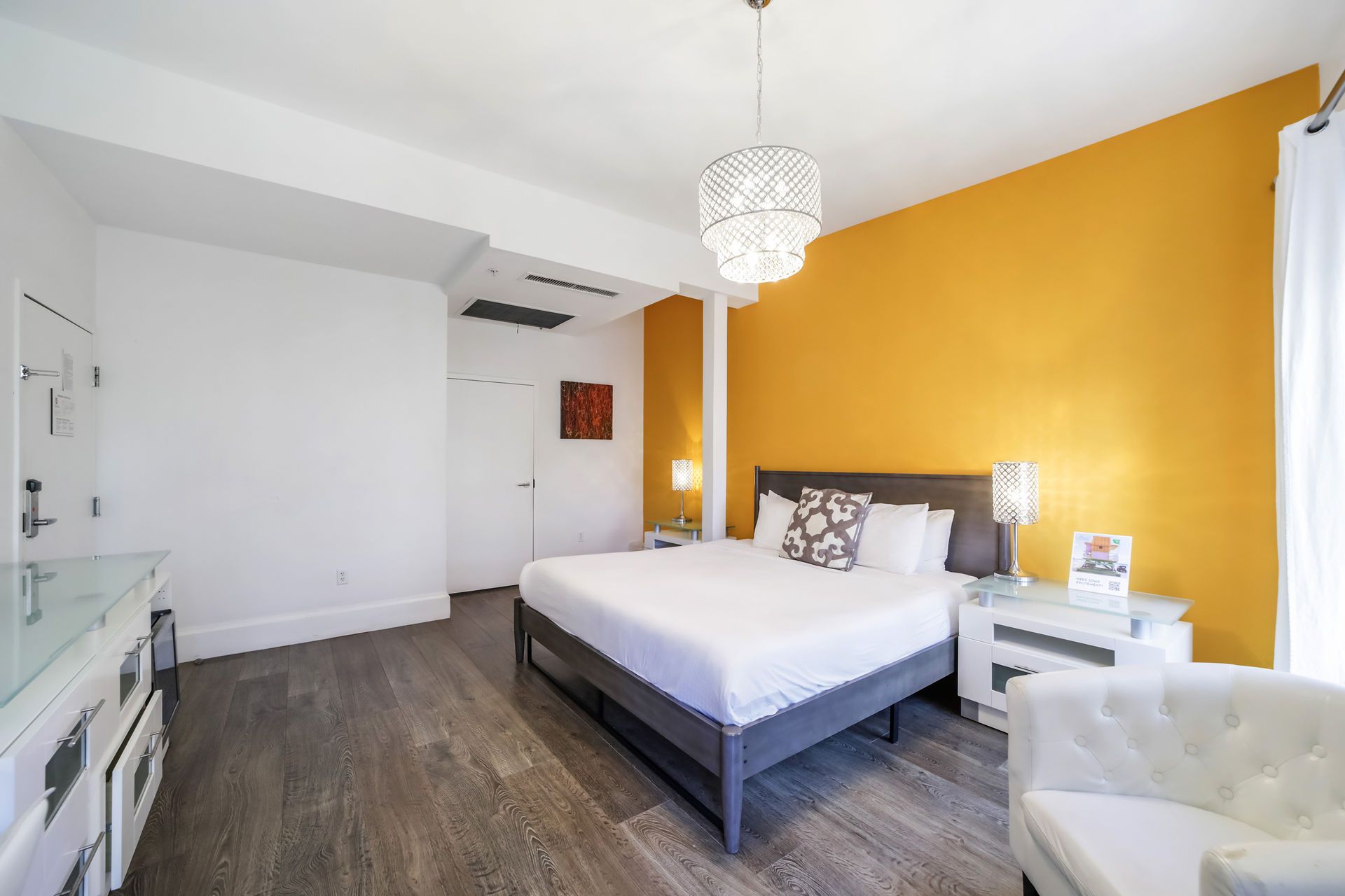 Bedroom with an orange accent wall, bed, white nightstands, and a small white armchair.
