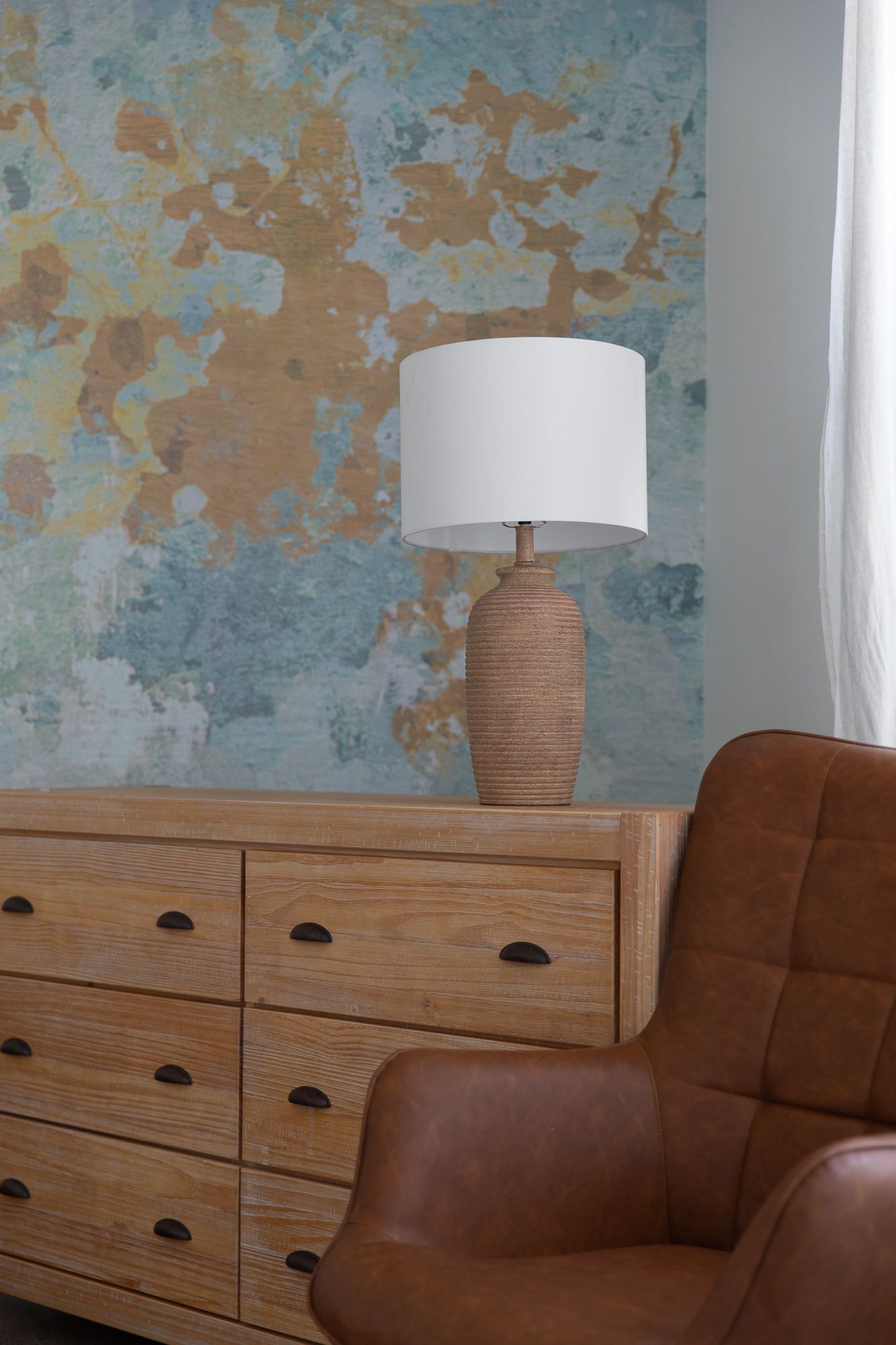 Rustic dresser with lamp beside a brown leather chair and textured blue wall