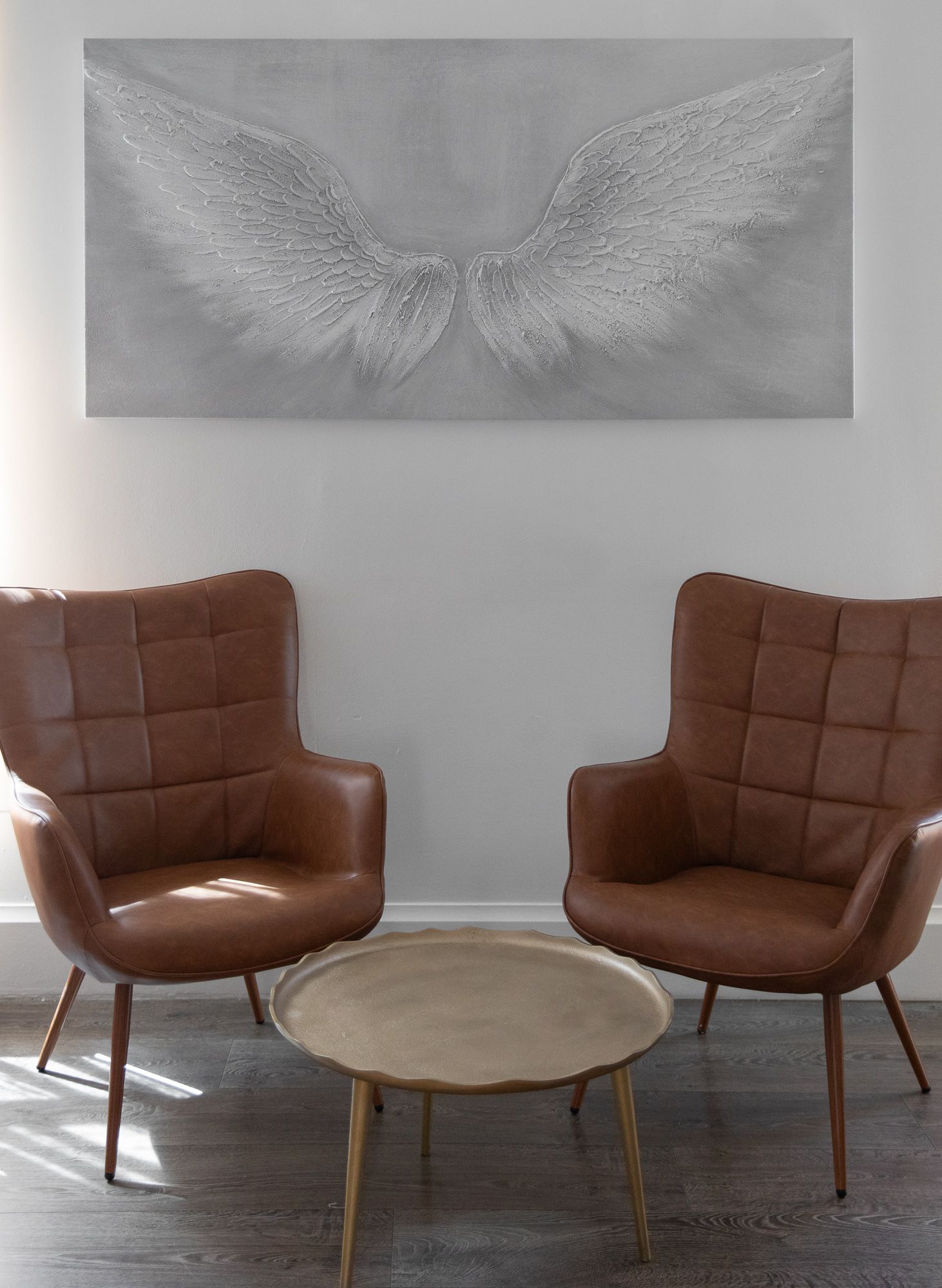 Two brown leather chairs and a round coffee table beneath a large silver abstract wall art piece.