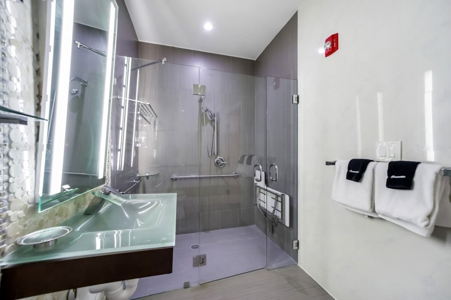 Modern bathroom with glass shower, green sink, mirror, and towels on the wall