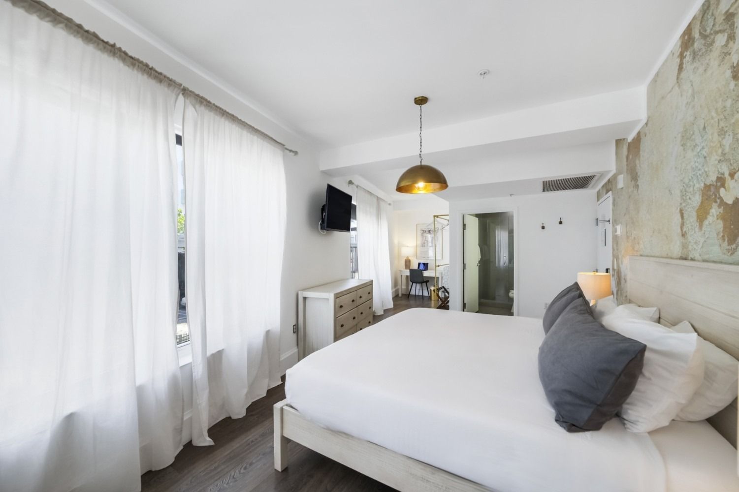 Bright bedroom with a large bed, white curtains, wall art, and a TV on the left.