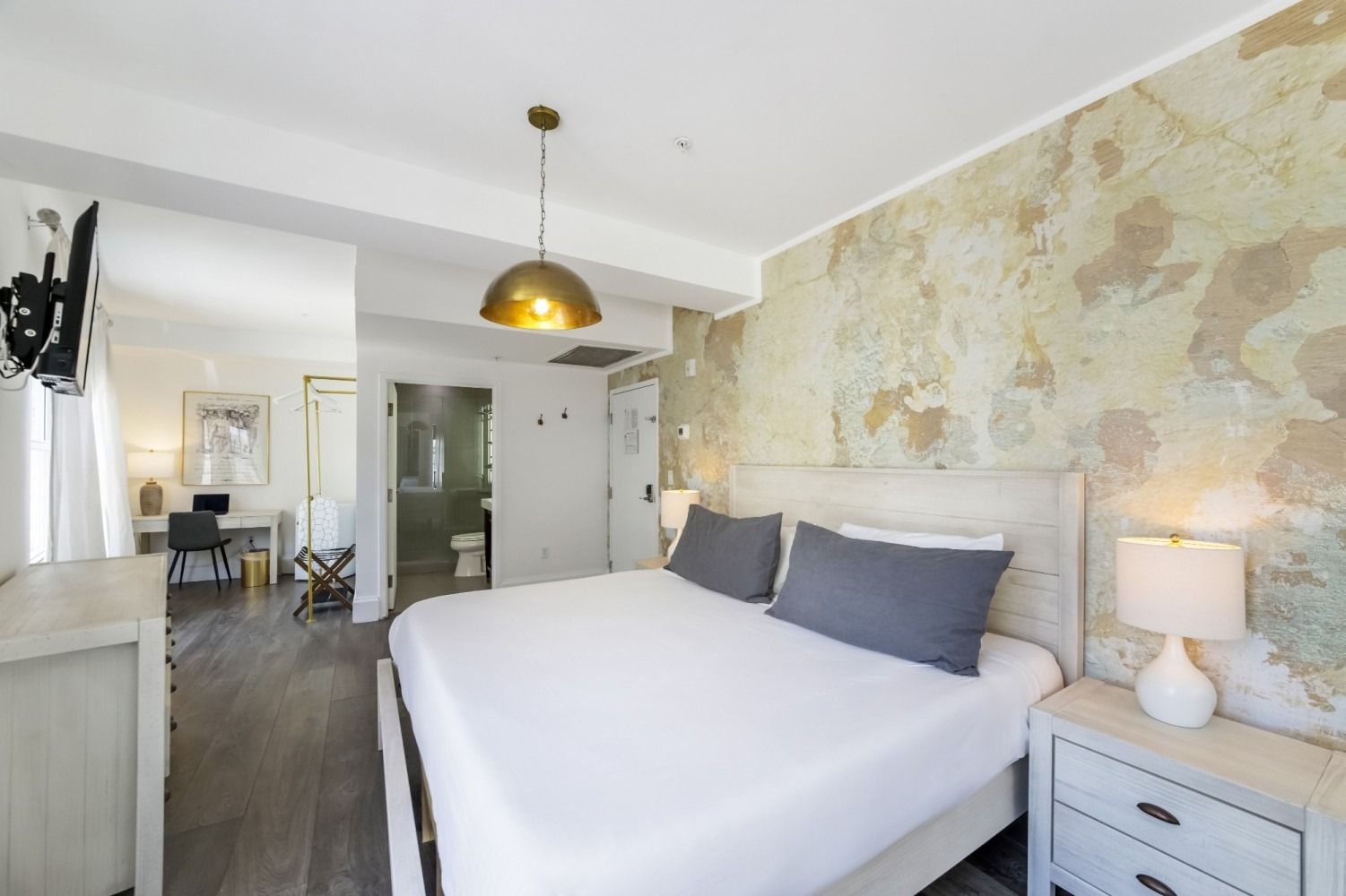 Bright bedroom with a white bed, gray pillows, bedside lamp, and map wallpaper accent wall