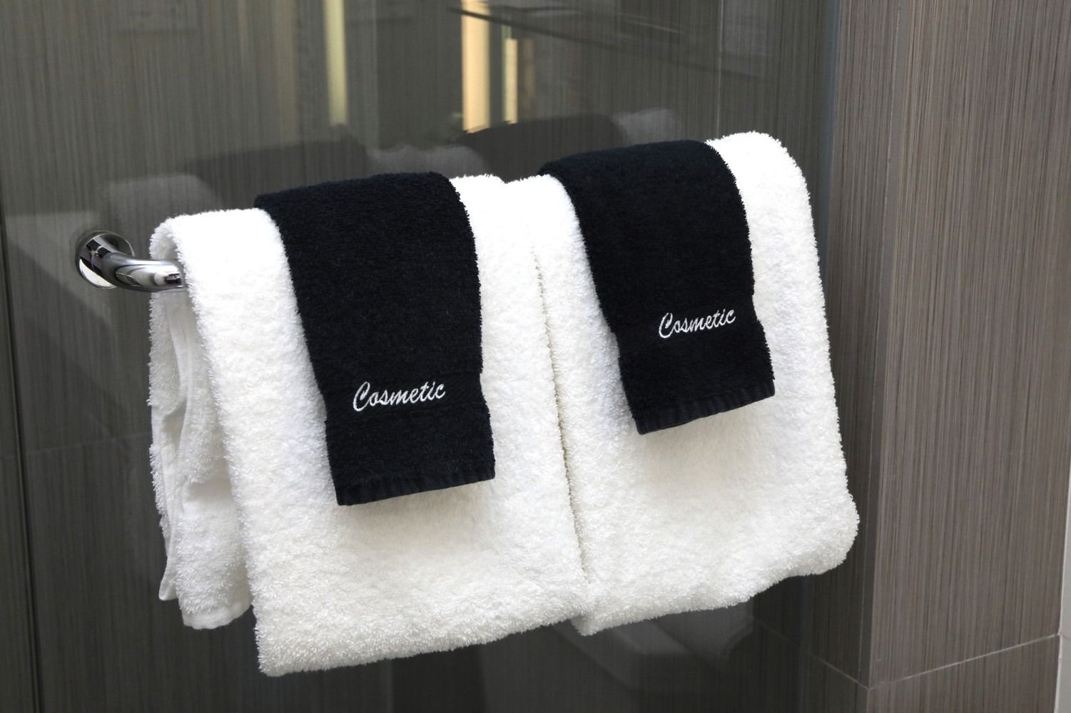 Two white towels hanging on a wall rack, each with a black embroidered label.