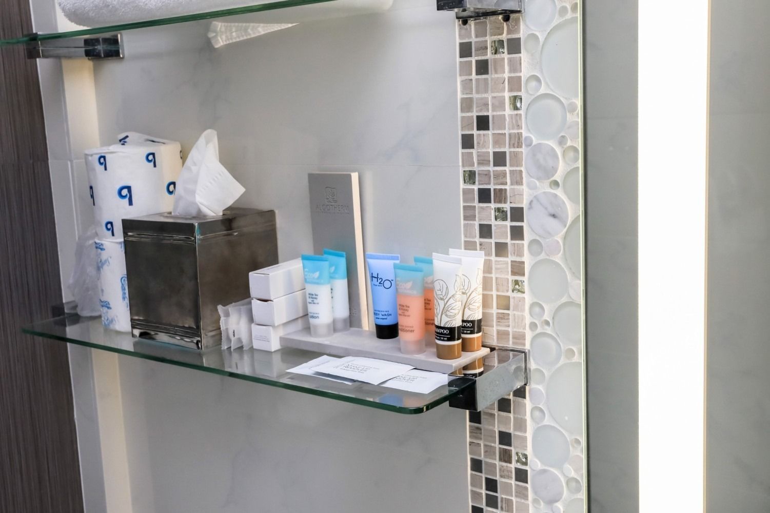 Bathroom shelves with assorted toiletries and folded tissue boxes on glass racks