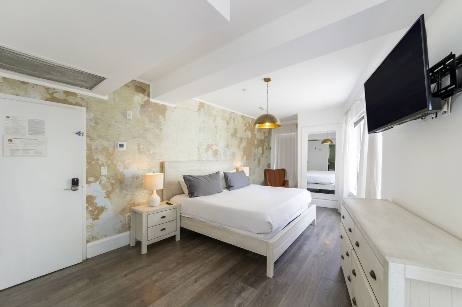 Bright modern bedroom with white bed, stone accent wall, and wall-mounted TV