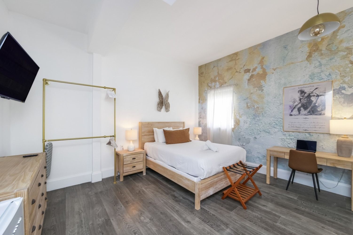 Bright bedroom with a wooden bed, patterned accent wall, desk, dresser, and TV mounted on the left wall