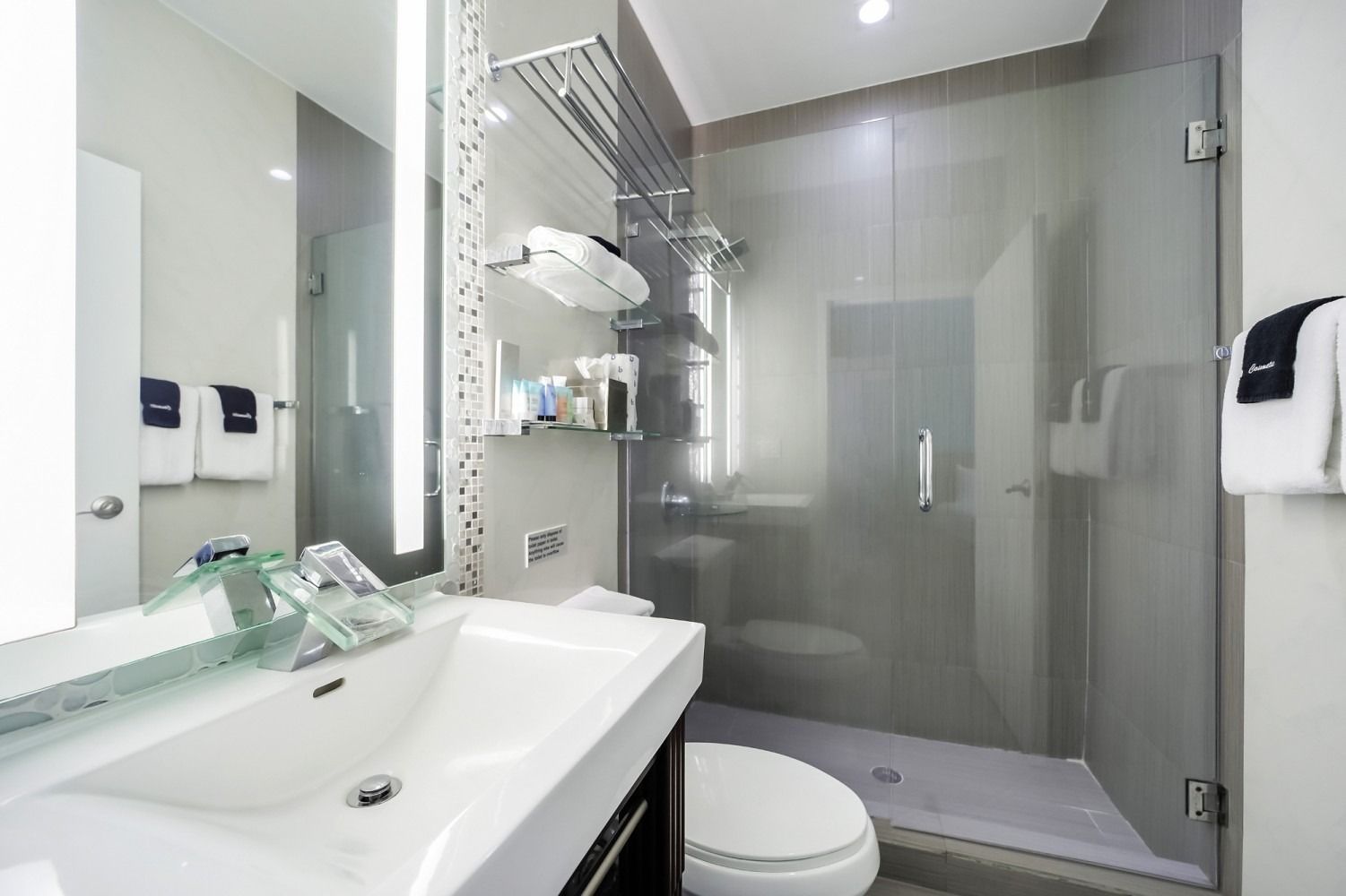 Modern bathroom with white sink, toilet, glass shower, and gray tile walls