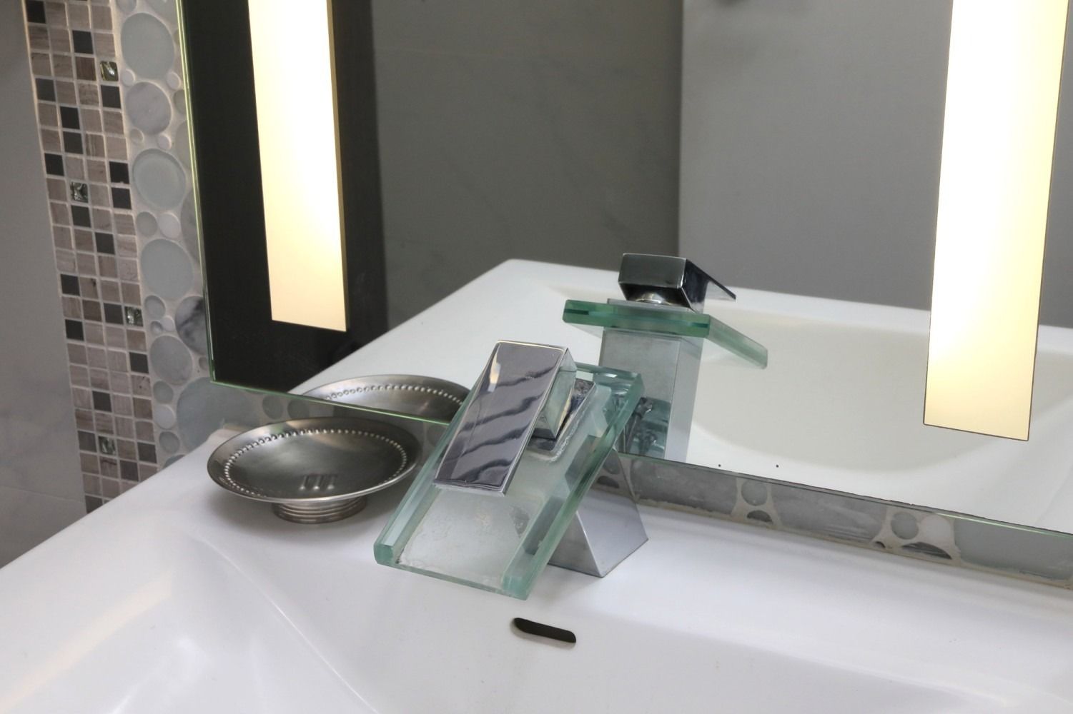 Modern bathroom sink with glass faucet, round bowl, and lit wall mirrors