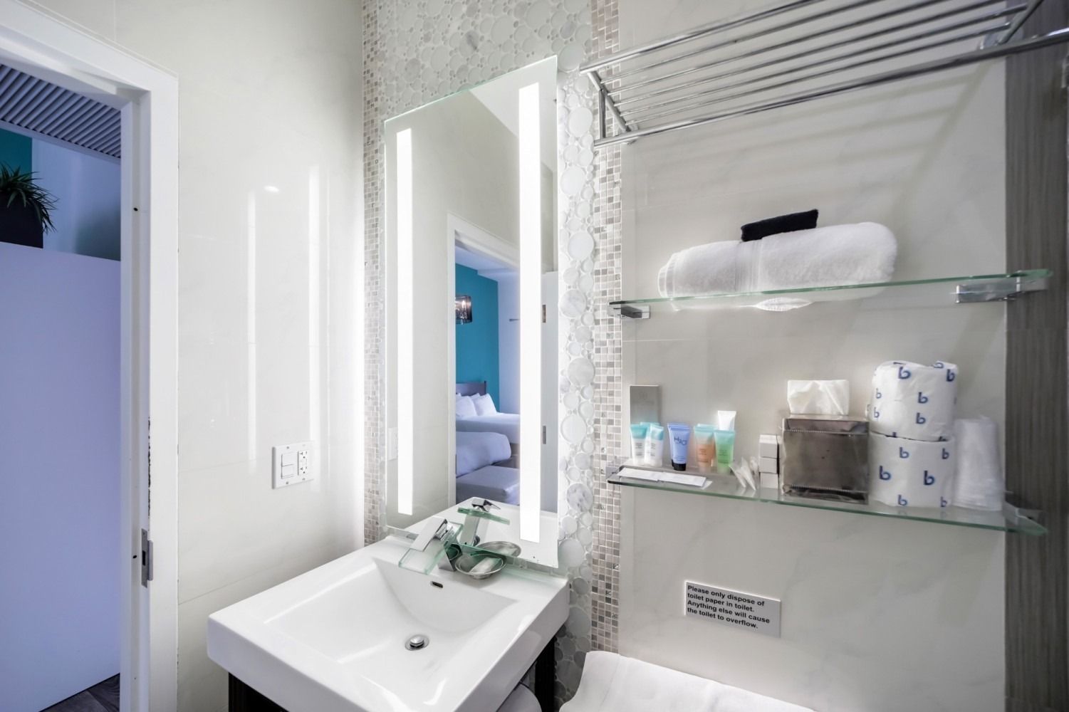 Modern white bathroom with sink, mirror, glass shelves, and toiletries; blue room visible through doorway