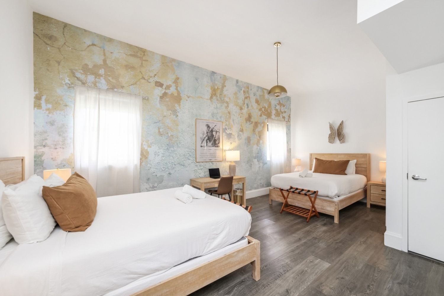 Bright bedroom with two white beds, floral accent wall, and dark wood floors