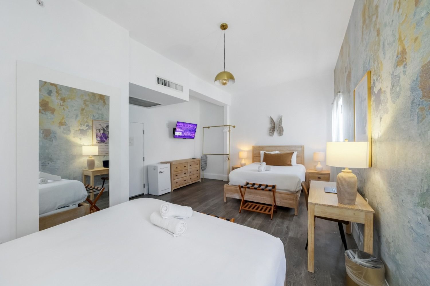 Bright hotel room with two beds, TV, mirror, and warm lamp lighting