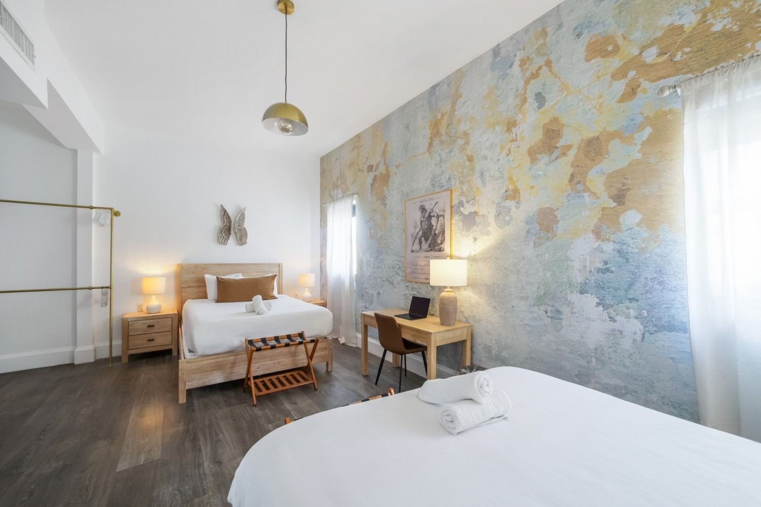 Bright bedroom with two beds, floral mural wall, wooden desk, and soft natural light