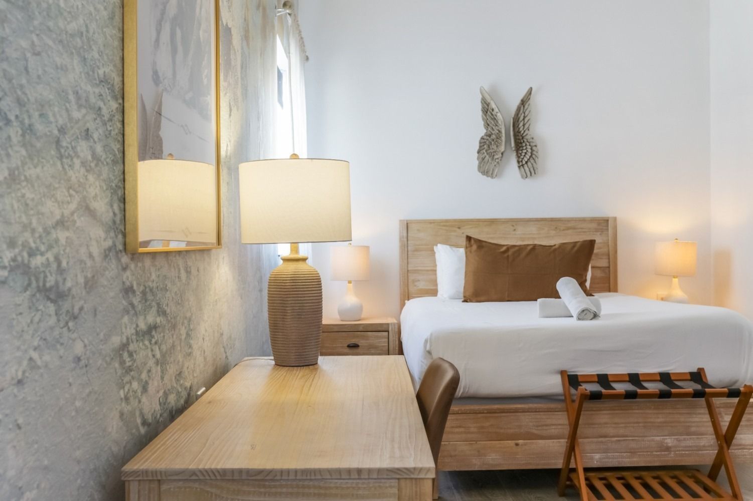 Cozy bedroom with bed, wooden desk, lamps, and textured wall art in soft neutral tones