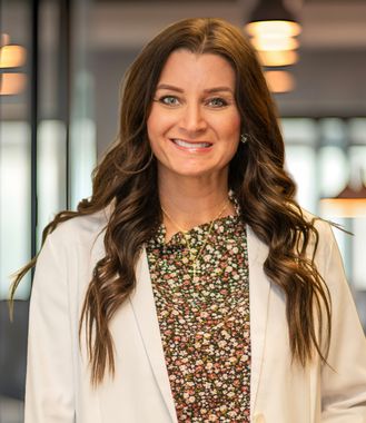 Smiling woman in a white blazer and floral top standing in a blurred office setting