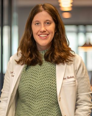 Woman in a white coat and green sweater smiling in a softly lit indoor setting