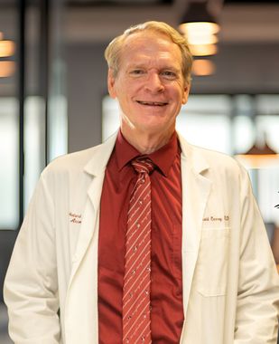 Doctor in a white coat and red tie standing indoors, smiling at the camera.