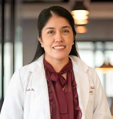 Portrait of a smiling doctor in a white coat and maroon blouse, standing in a clinic