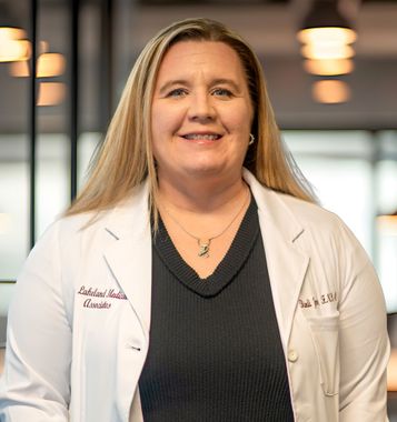 Smiling clinician in a white coat standing indoors in front of blurred lights