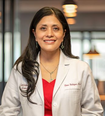 Woman in a white coat and red blouse smiling in a hospital hallway