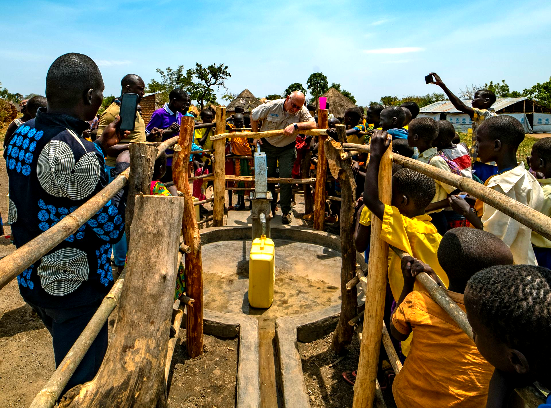 A man demonstrates a water pump to children in a village, likely in Africa.
