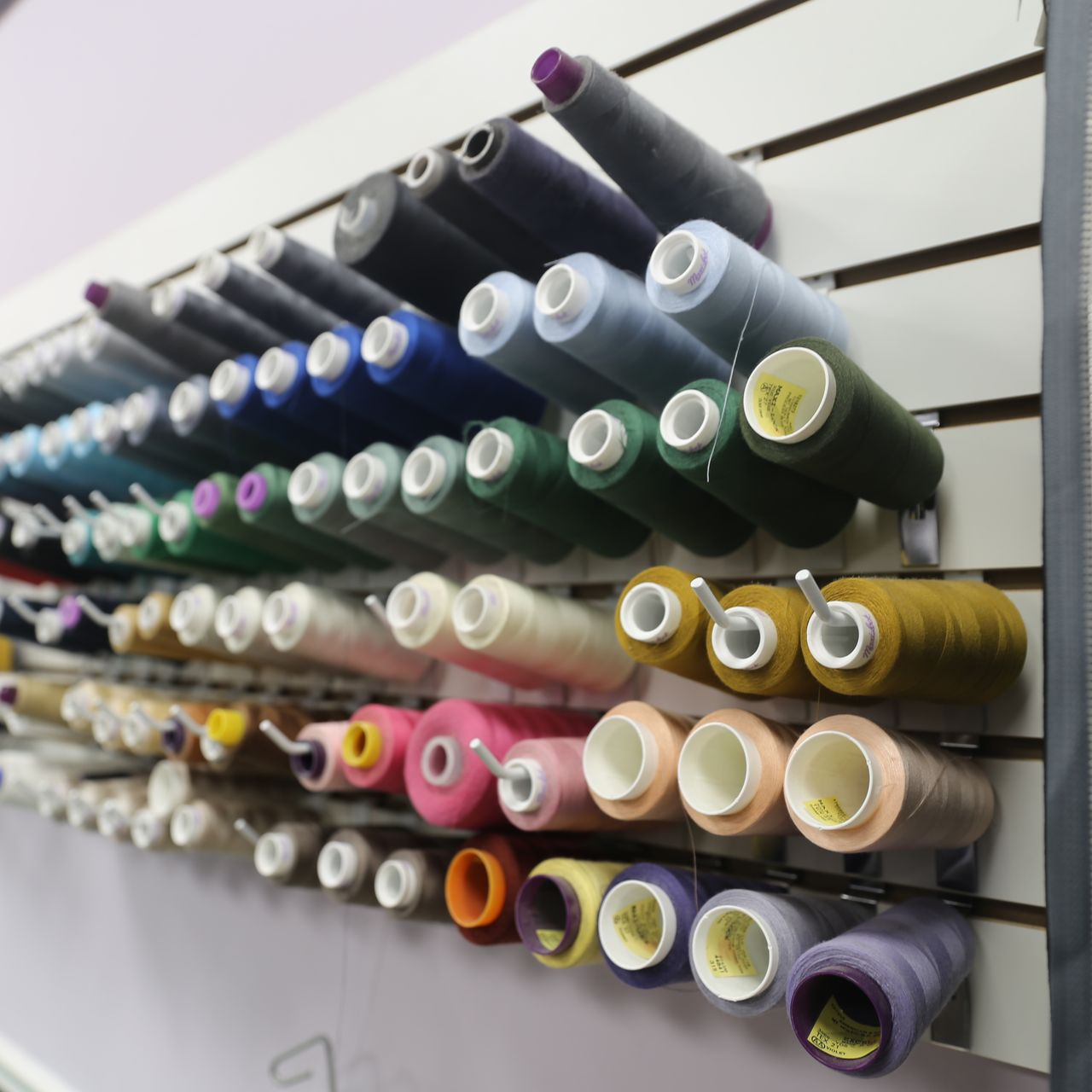 Spools of colorful thread organized on a wall-mounted rack.
