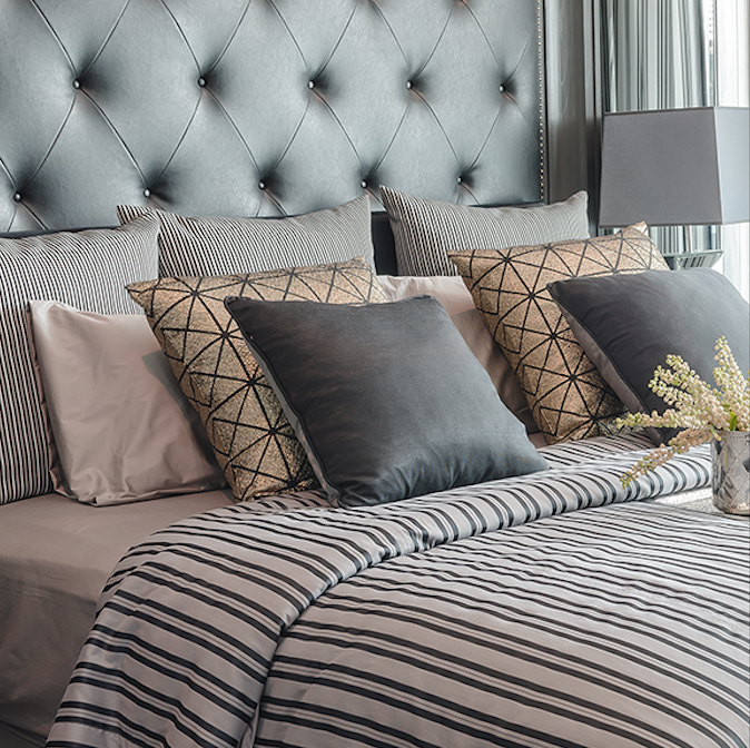 Bed with gray tufted headboard, striped comforter, and various decorative pillows.