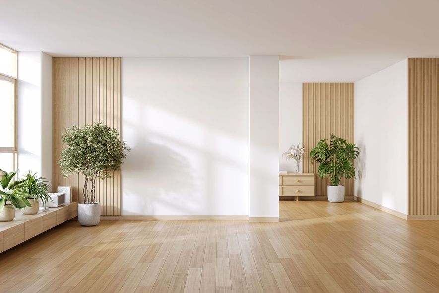 A bright, minimalist room with light wood floors, white walls, vertical wood paneling, and two potted green plants.