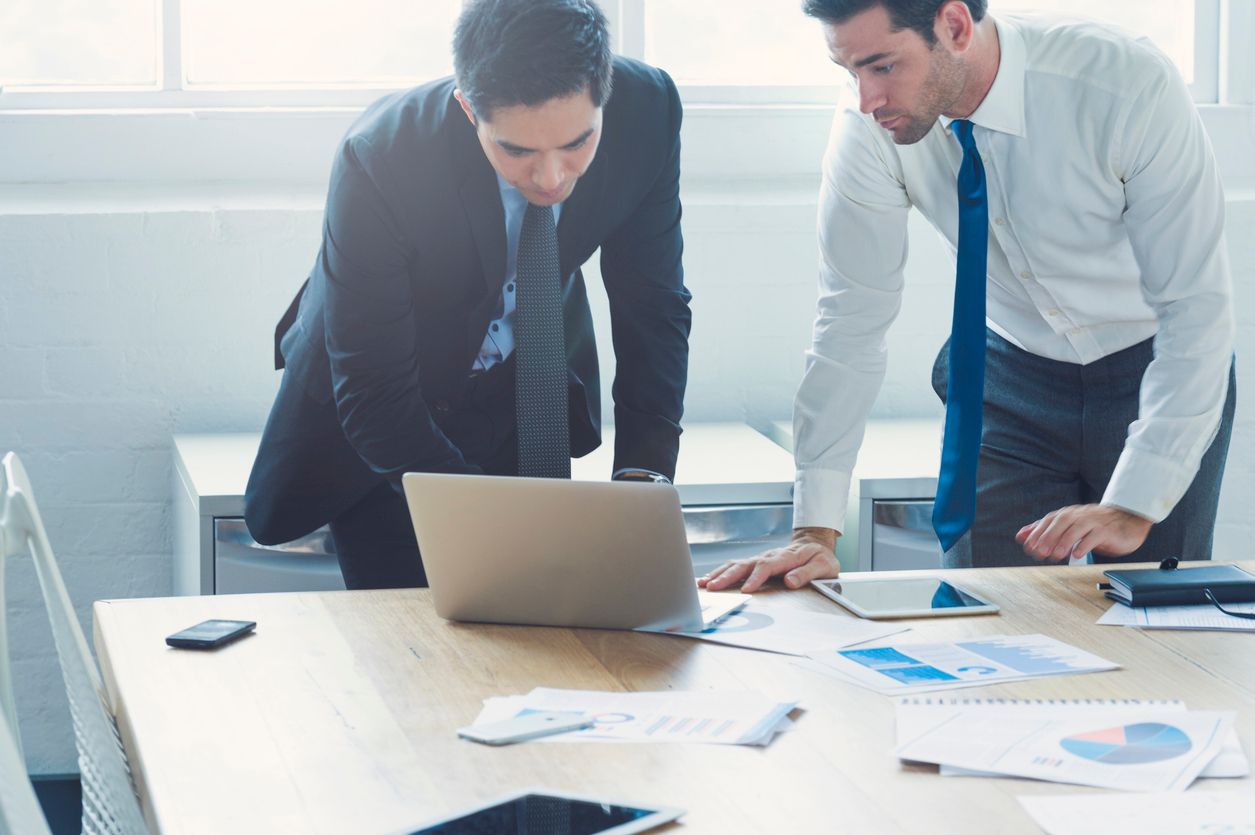 Two company directors reviewing financial reports and tax documents at a desk with a laptop and charts