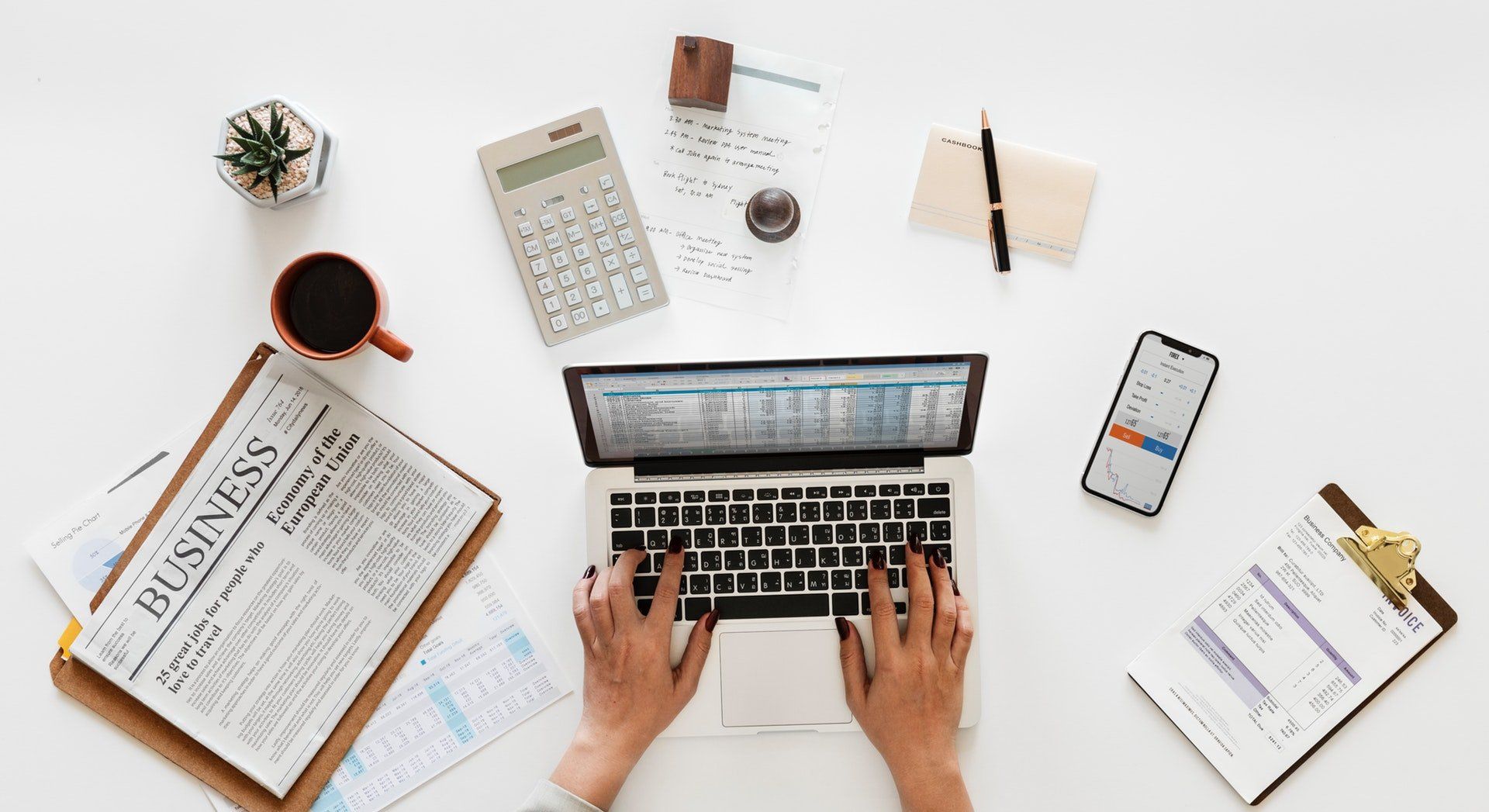 Laptop, a news paper, a calculator and mobile phone on a desk