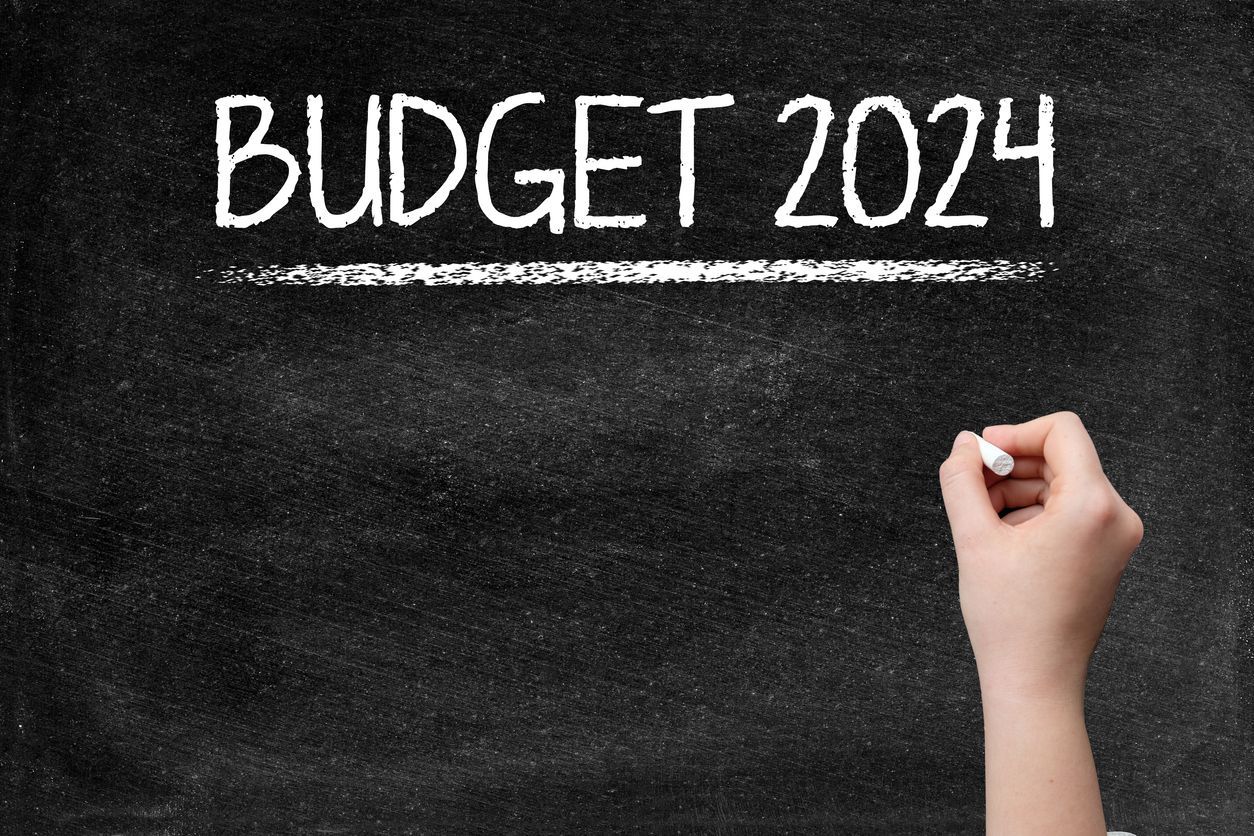 Chalk board with word Budget 2024 and a hand holding chalk