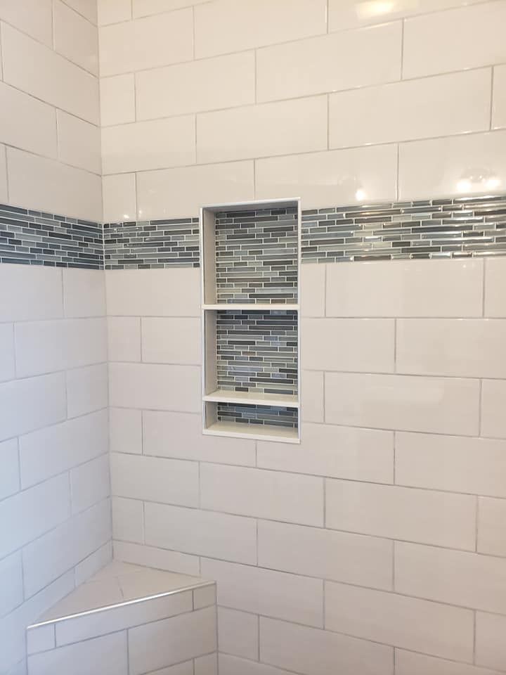 White tiled shower with mosaic accent and built-in shelves.