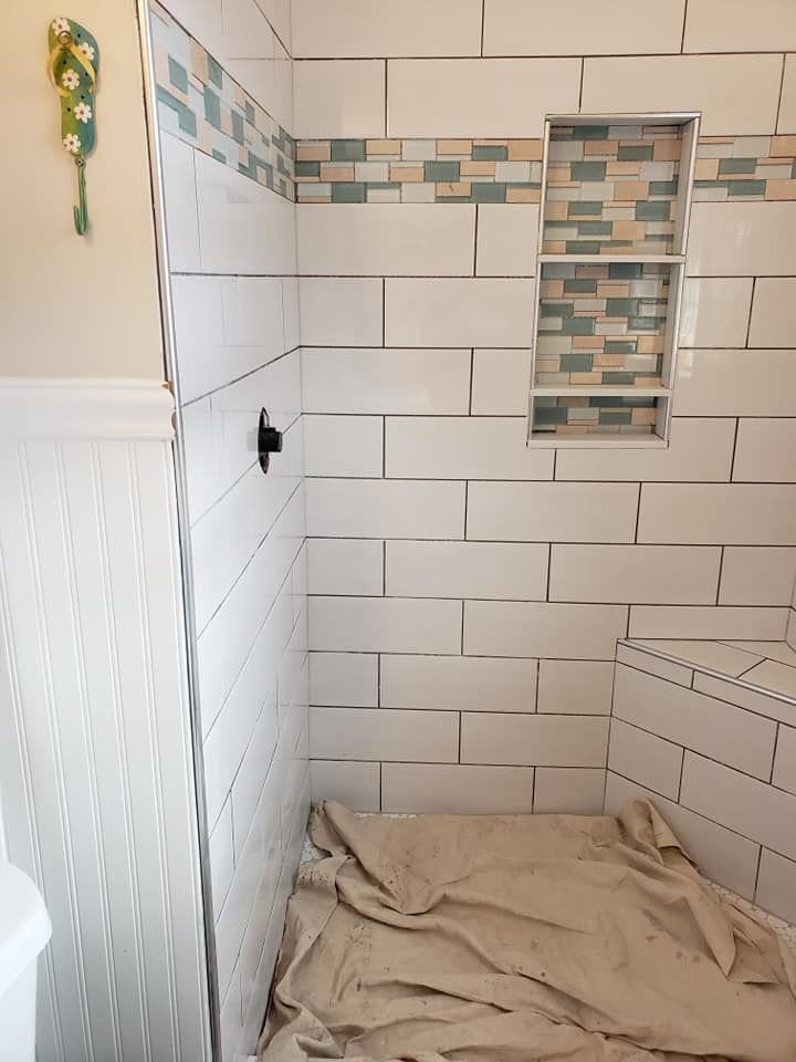 White tiled shower with a decorative blue tile border and a built-in shelf.