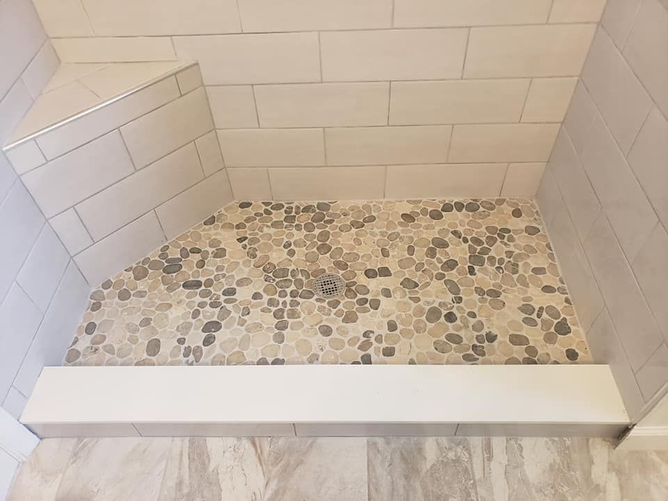 Shower stall with a pebble tile floor and built-in seat; white and gray tones.