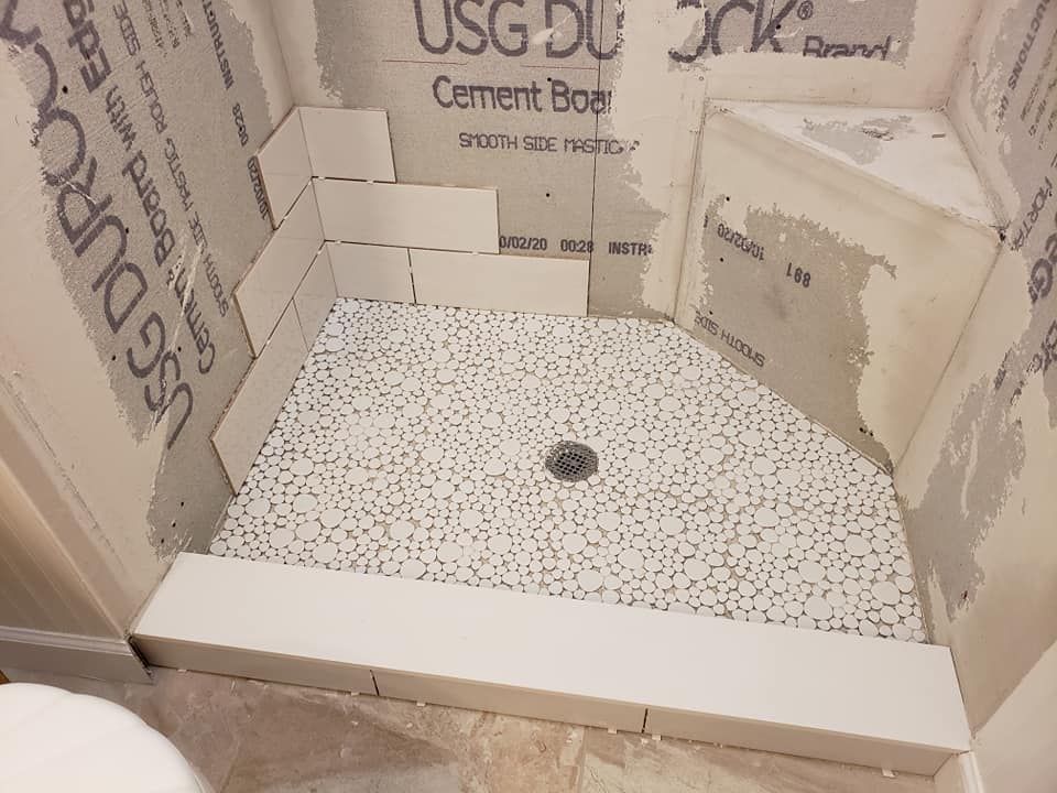 A partially tiled shower with a mosaic tile floor and cement board walls.