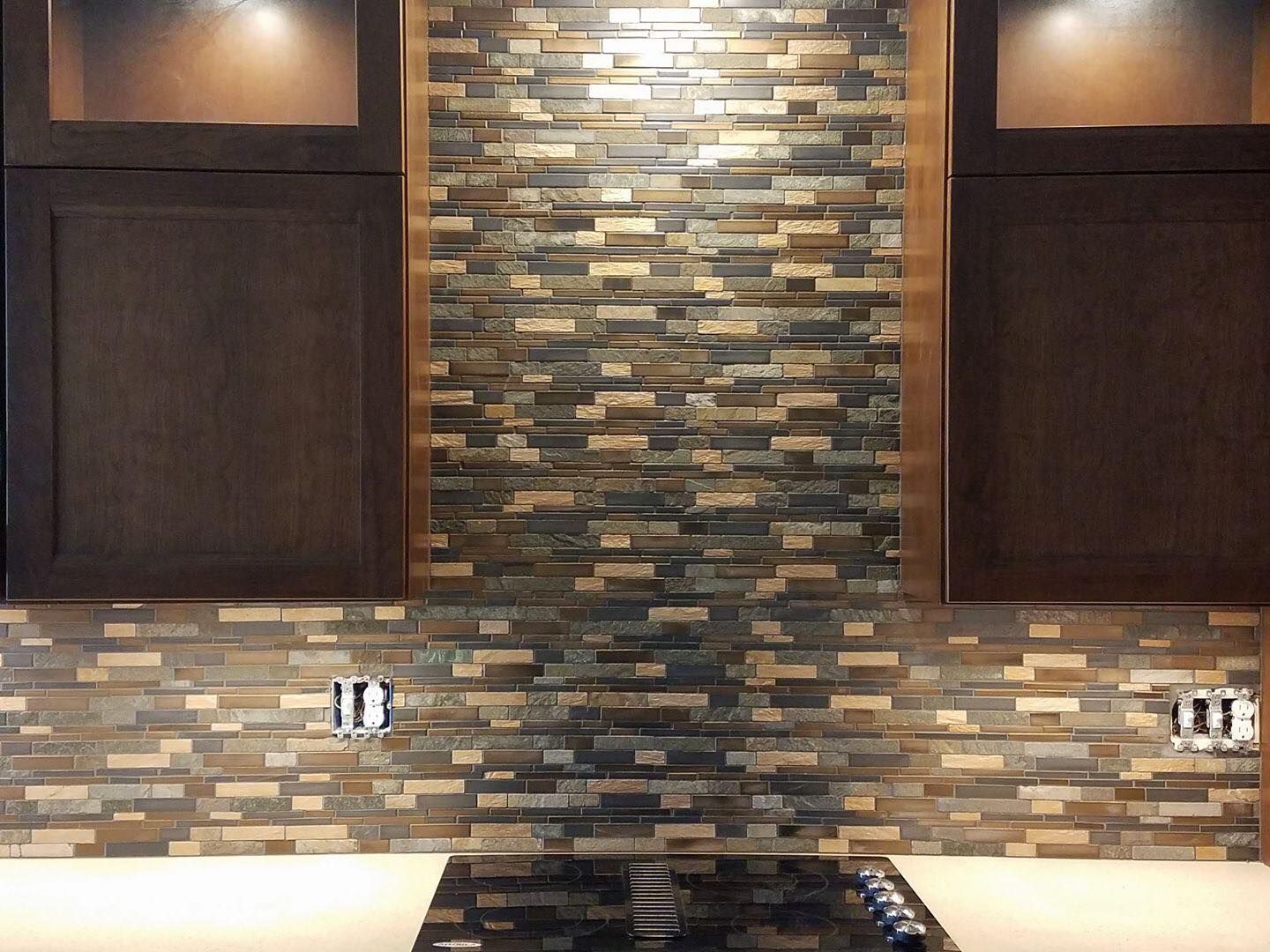 Dark kitchen cabinets frame a textured stone backsplash above a stove, with accent lighting.