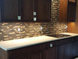 Dark brown kitchen cabinets with light countertops and a stone backsplash.