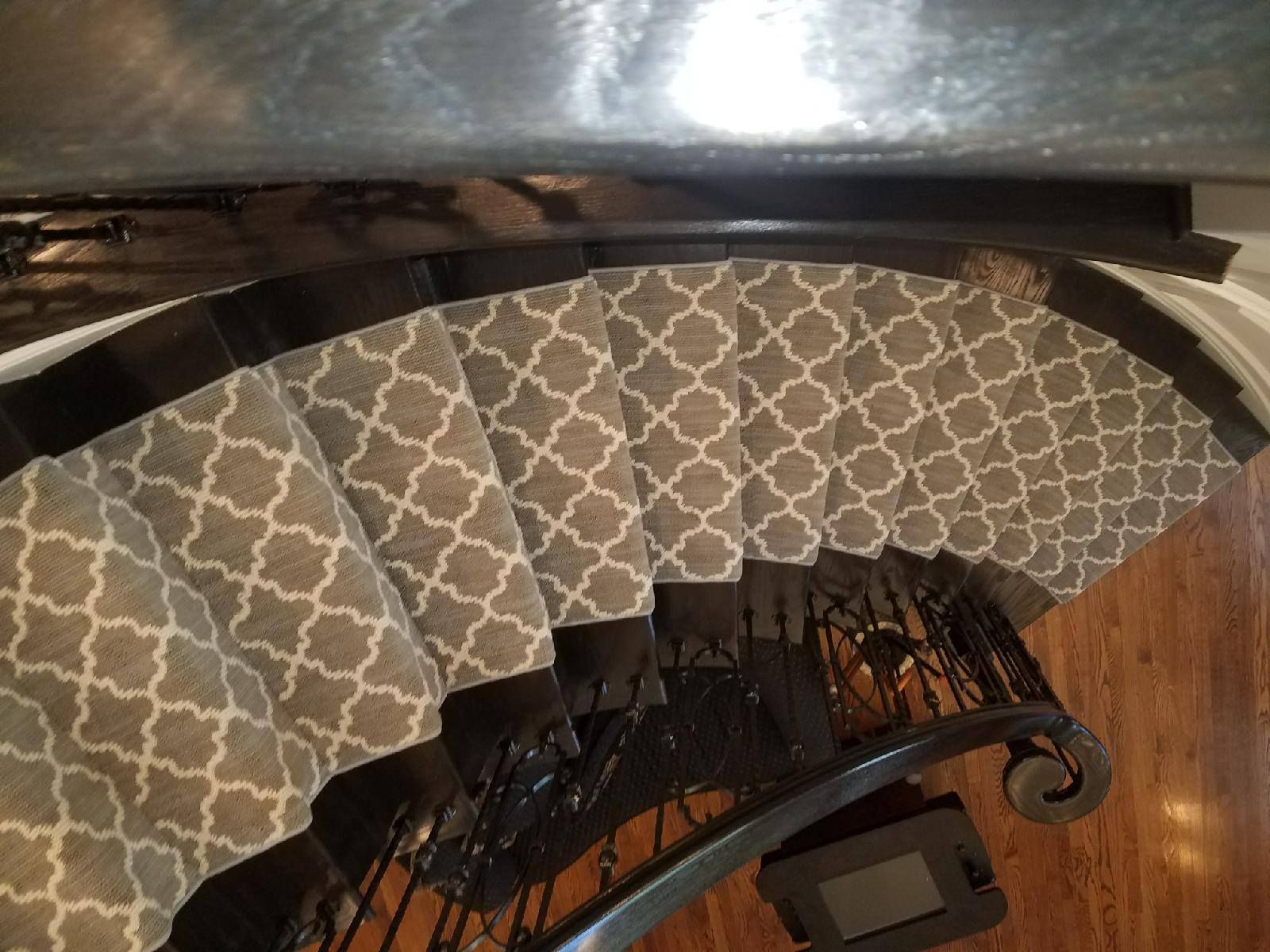 Staircase with gray patterned carpet and black banister winding down to a hardwood floor.