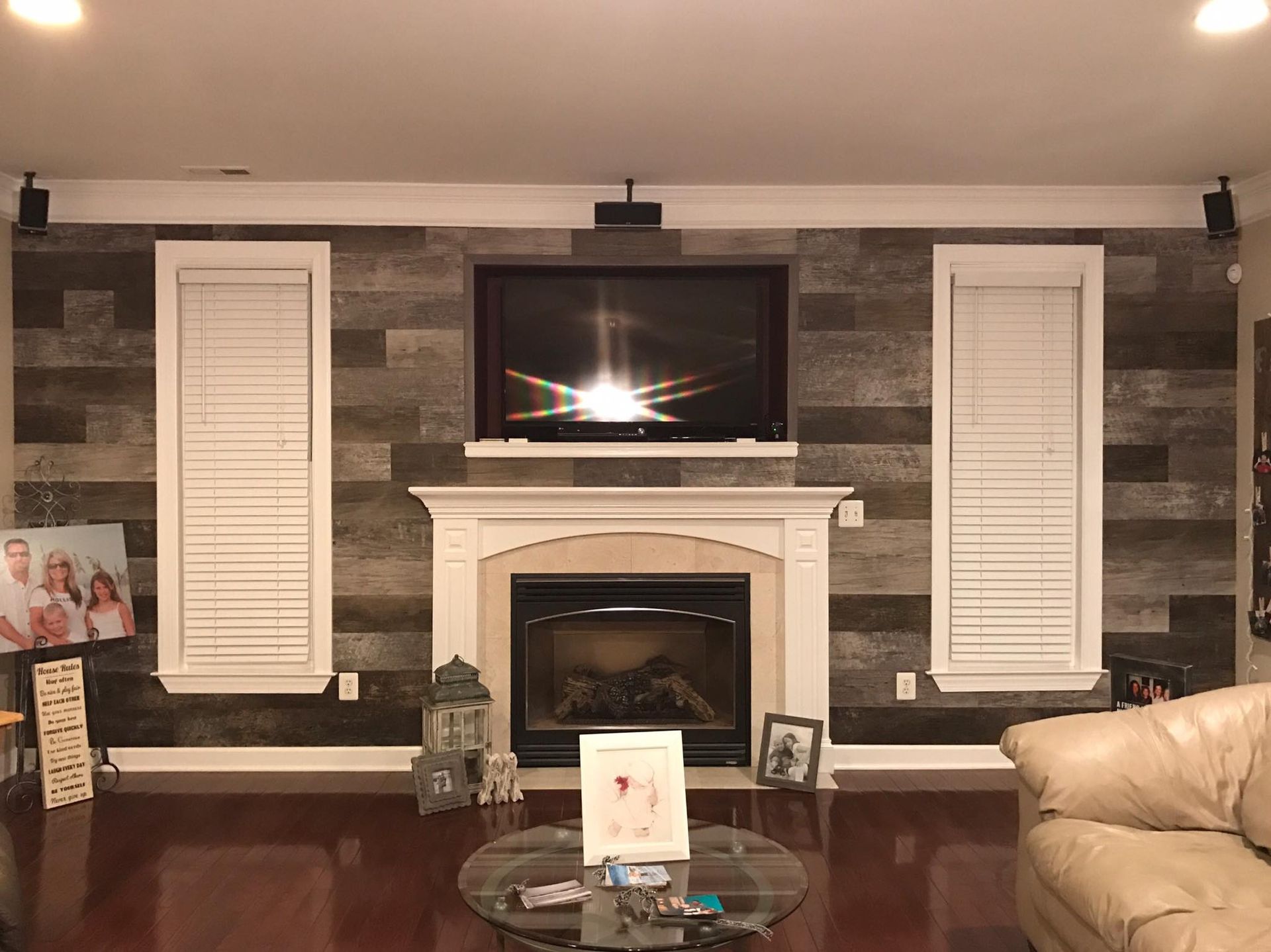Living room with fireplace, TV, wood panel wall, and two windows with blinds.
