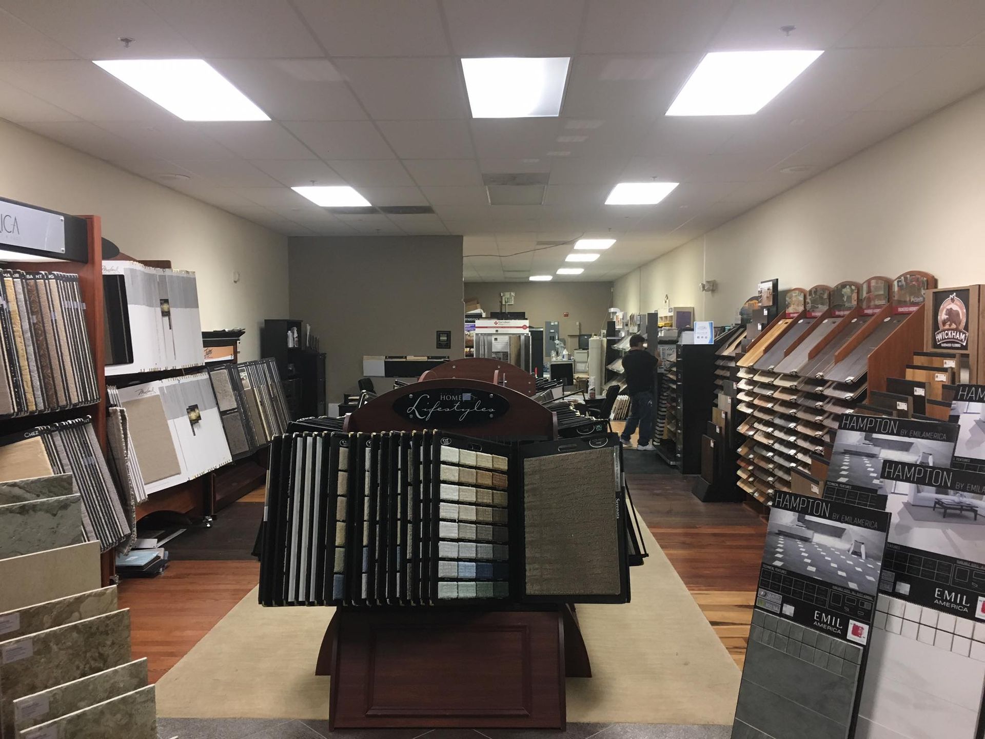 Interior of a flooring store with rows of tile and carpet samples displayed on racks and tables.