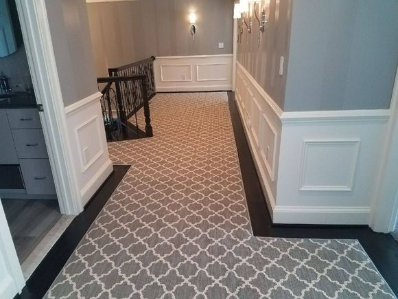 Hallway with gray patterned rug, white wainscoting, black trim, and a staircase.