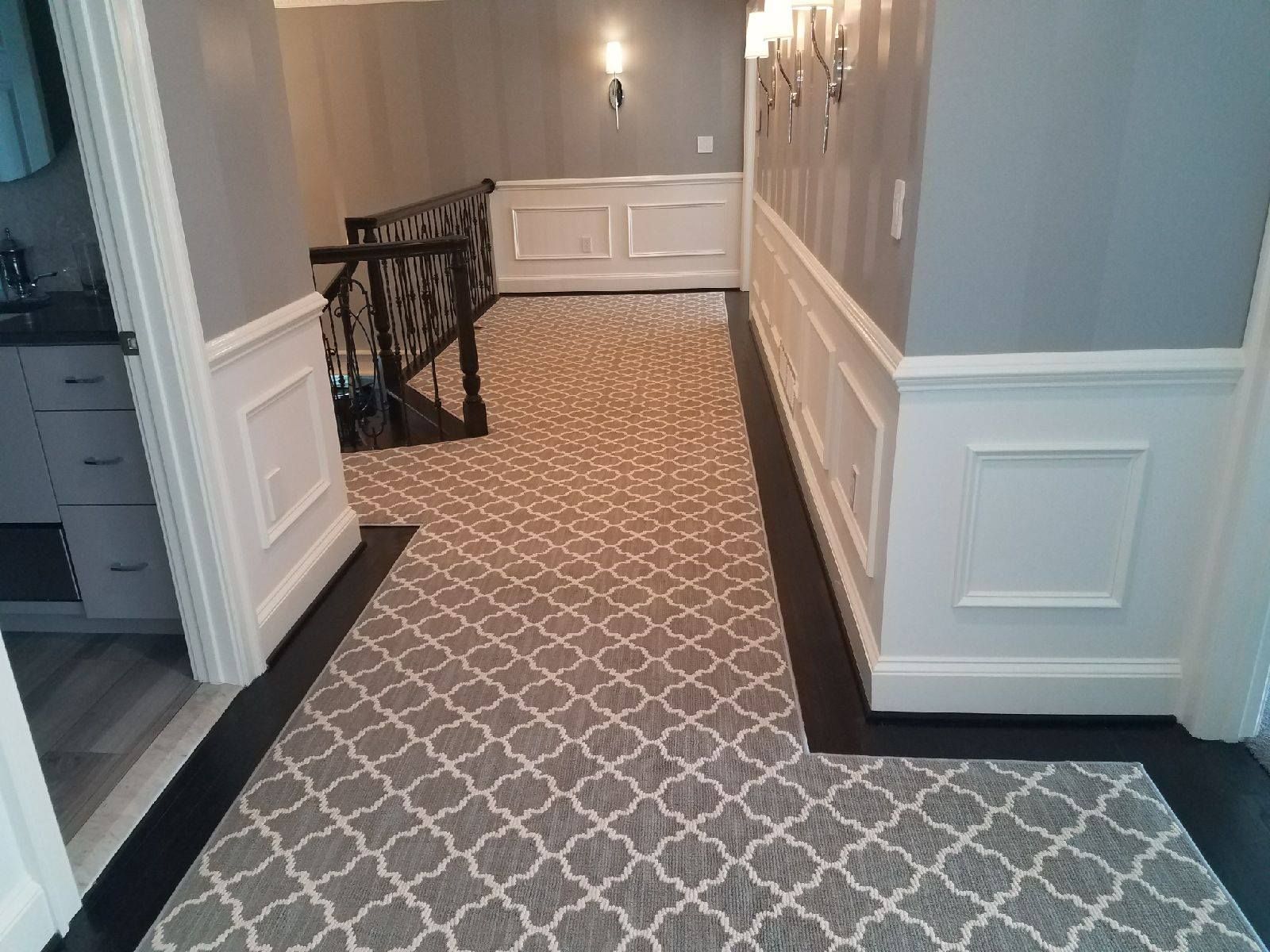 Hallway with patterned rug, dark wood trim, white wainscoting, and grey walls.