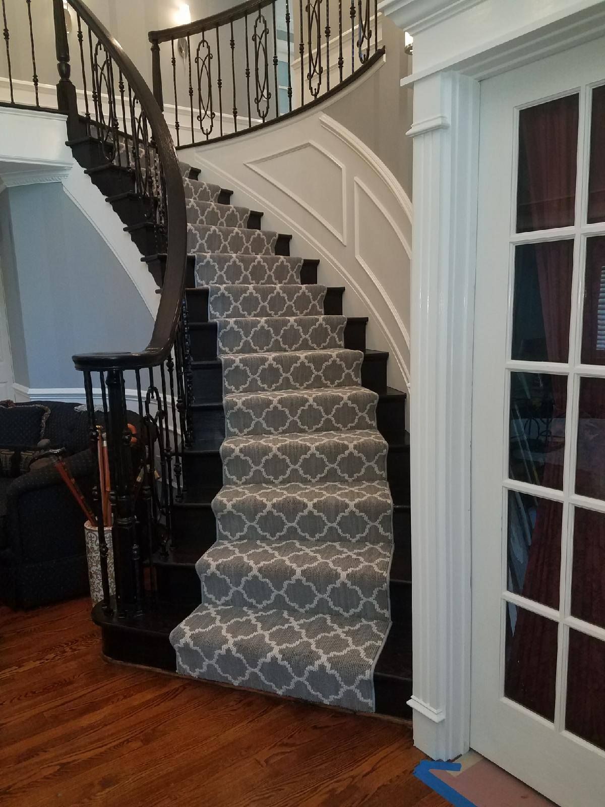 A grand curved staircase with grey patterned carpet and dark wood, next to a white door.