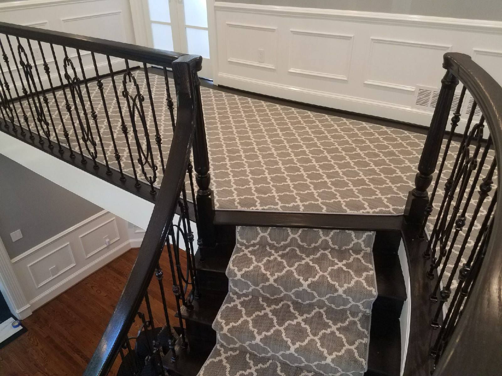 Staircase with patterned carpet, dark wood railing, and white wainscoting.