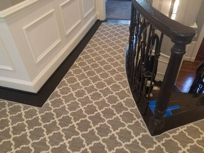 Hallway with patterned carpet, white walls, dark wood trim, and a staircase with a black banister.