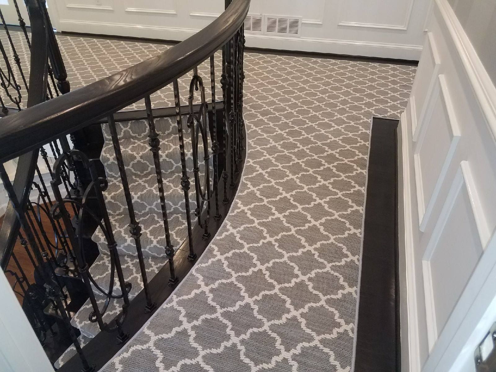 Gray patterned carpeted stairs with dark railing, leading downwards.