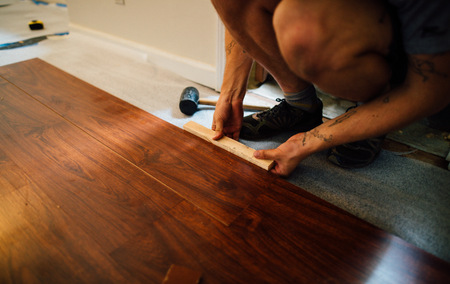 Person installing hardwood flooring, kneeling, using a block and hammer.